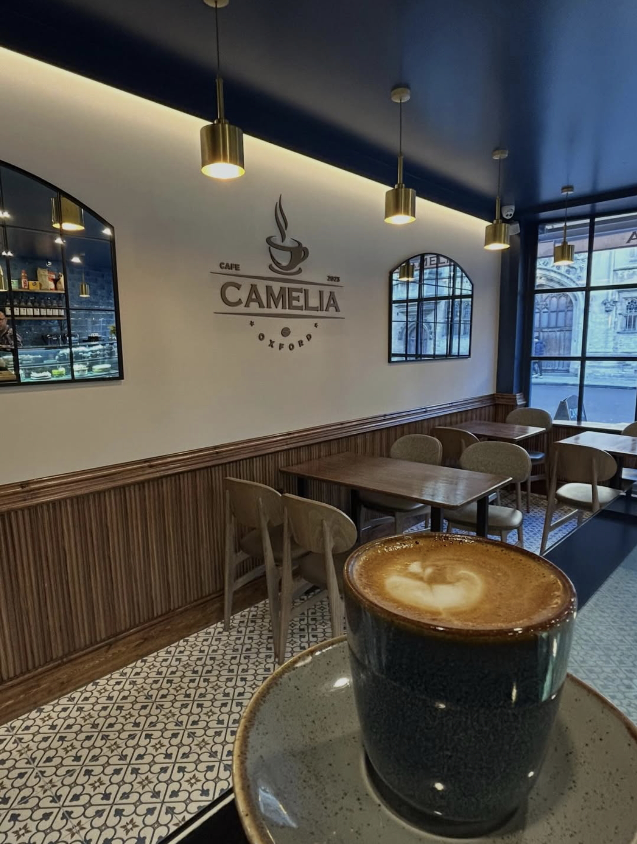 Inside Camelia Patisserie & Cafe — pendant lights, navy ceiling, and a flat white on patterned tile